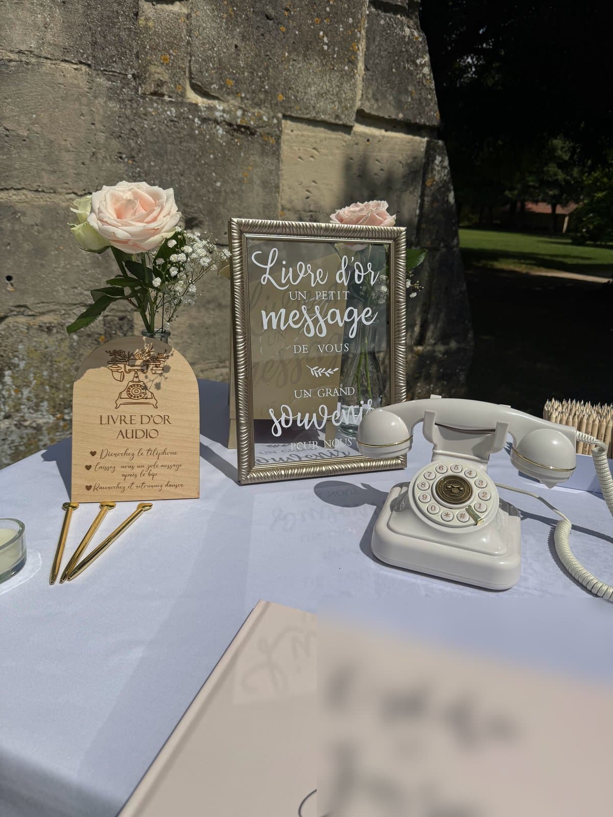 Livre d'or audio : téléphone rétro blanc sur une table de mariage, à côté d'un cadre « Livre d'or » et de roses