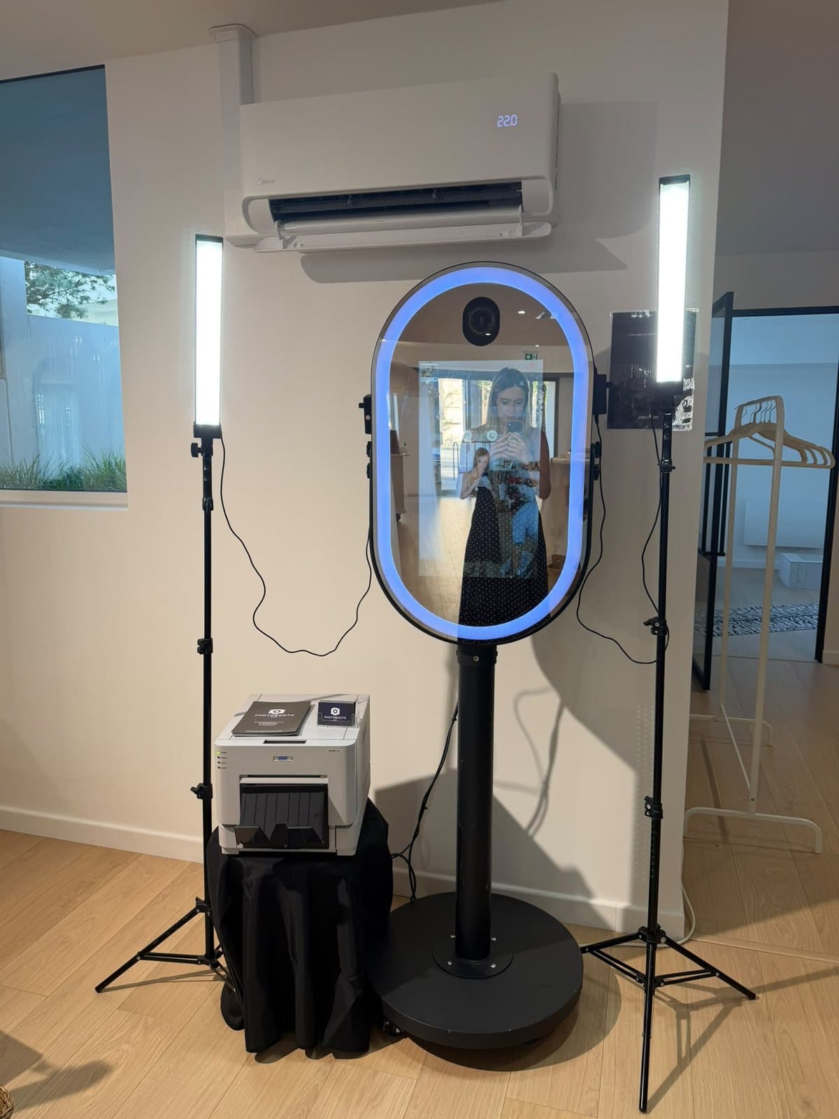 Photobooth miroir installé dans une salle, contour lumineux bleu, entre deux éclairages LED, avec son imprimante DNP