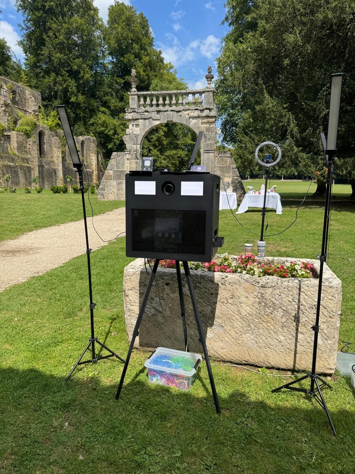 Photobooth classique noir installé dans le parc d'un château, entre deux éclairages LED, devant une arche en pierre